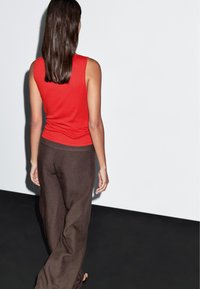 Un top sans manches rouge associé à un pantalon en lin marron ample. Le tissu semble doux avec une coupe décontractée, présentant un design simple.