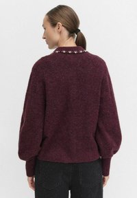 Burgundowy miękki sweter o luźnym kroju z balonowymi rękawami i perłowymi akcentami na kołnierzu; teksturowana powierzchnia oraz prążkowane mankiety.