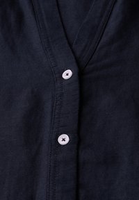 Camicia blu navy con scollatura a V, realizzata in tessuto testurizzato, con due bottoni a contrasto visibili sulla patta.