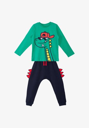 Haut vert à manches longues avec un dinosaure portant une casquette rouge et des lunettes de soleil, associé à un pantalon bleu marine avec des pointes de dinosaure rouges sur les côtés.