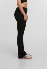 Jeans negros de campana con una cintura de altura media, que presentan una textura suave y un detalle mínimo. Combinados con zapatillas blancas y beige.