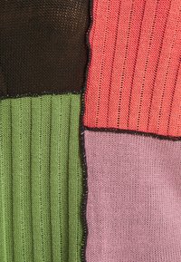 Tissu tricoté en patchwork avec des sections vertes, noires, roses et corail cousues ensemble avec un fil noir.