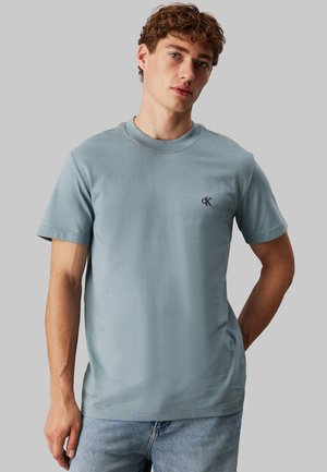 T-shirt di cotone azzurro chiaro con colletto tondo, maniche corte e logo “ck” sul petto sinistro. Design semplice con una texture liscia.