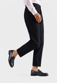 Pantaloni neri con un design affusolato, abbinati a mocassini scuri. I pantaloni presentano linee pulite e i mocassini hanno una finitura in pelle liscia.