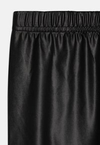 Los pantalones de satén negro cuentan con una cintura elástica y una textura suave y brillante. La tela cae suavemente con un ligero brillo y sin patrones visibles.