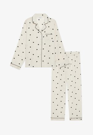Conjunto de pijama de dos piezas hecho de tela suave, con fondo crema y pequeños patrones de corazones negros, ribetes negros y cierre de botones.