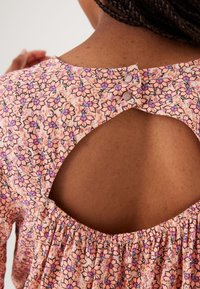 Bavlněný top s květinovým potiskem v broskvové barvě, s nabíraným výstřihem a odhaleným zadním dílem s dvěma knoflíky na zavírání na šíji.