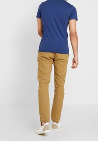 Marinblå t-shirt med kort ärm som matchas med slim-fit khakibyxor. Vita sneakers med beige detaljer. Enkel, slät tygtextur.