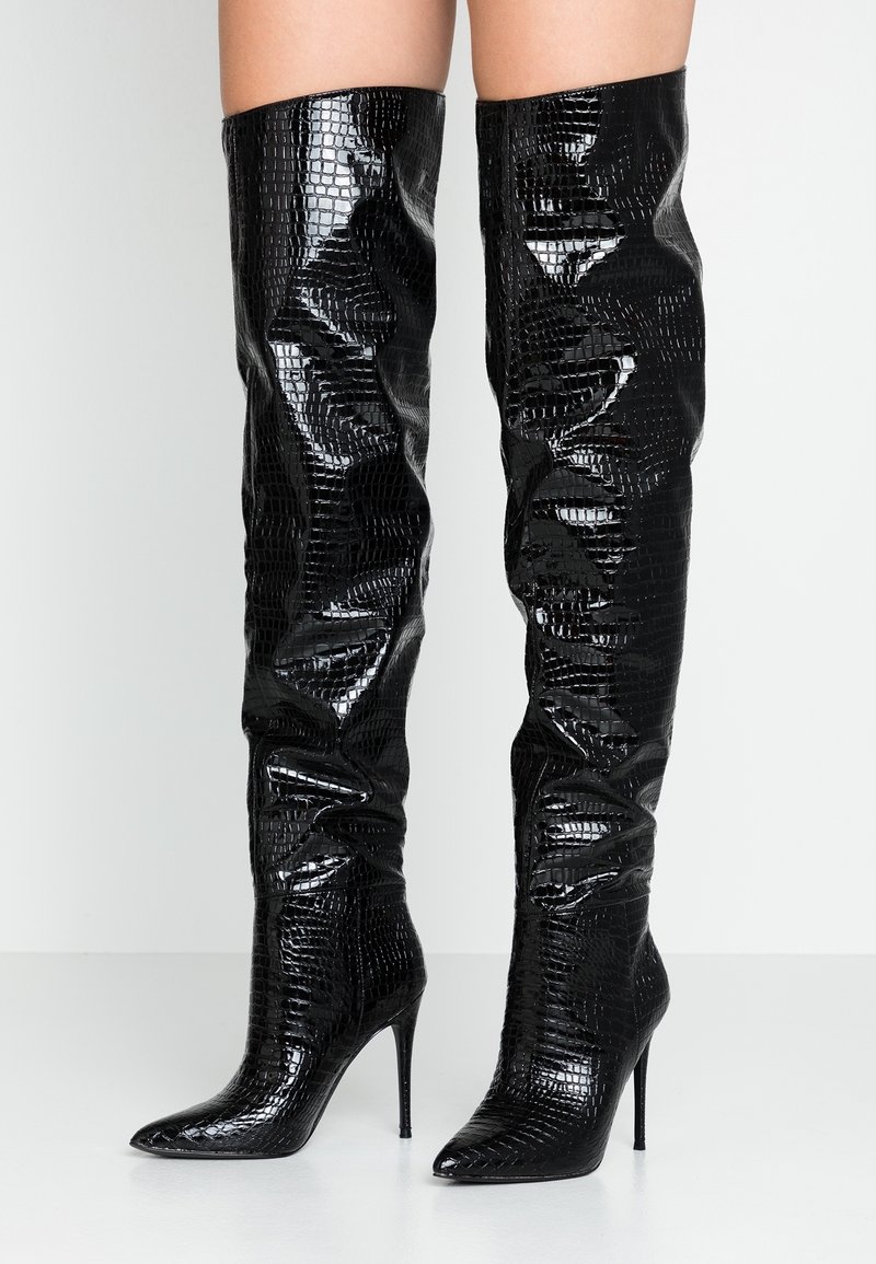 Botas negras sobre la rodilla con un patrón de cocodrilo texturizado y brillante, punta afilada y tacón de aguja alto. Parte superior suave con detalles fruncidos.
