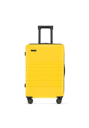 Yellow hard-shell suitcase with black accents, telescoping handle, four wheels, and textured side panels for stability.