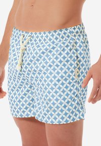 Șorturi de înot de culoare albastru deschis, cu un model geometric alb. Au un talie cu șnur și un buzunar lateral cu un mic etichetă a brandului.