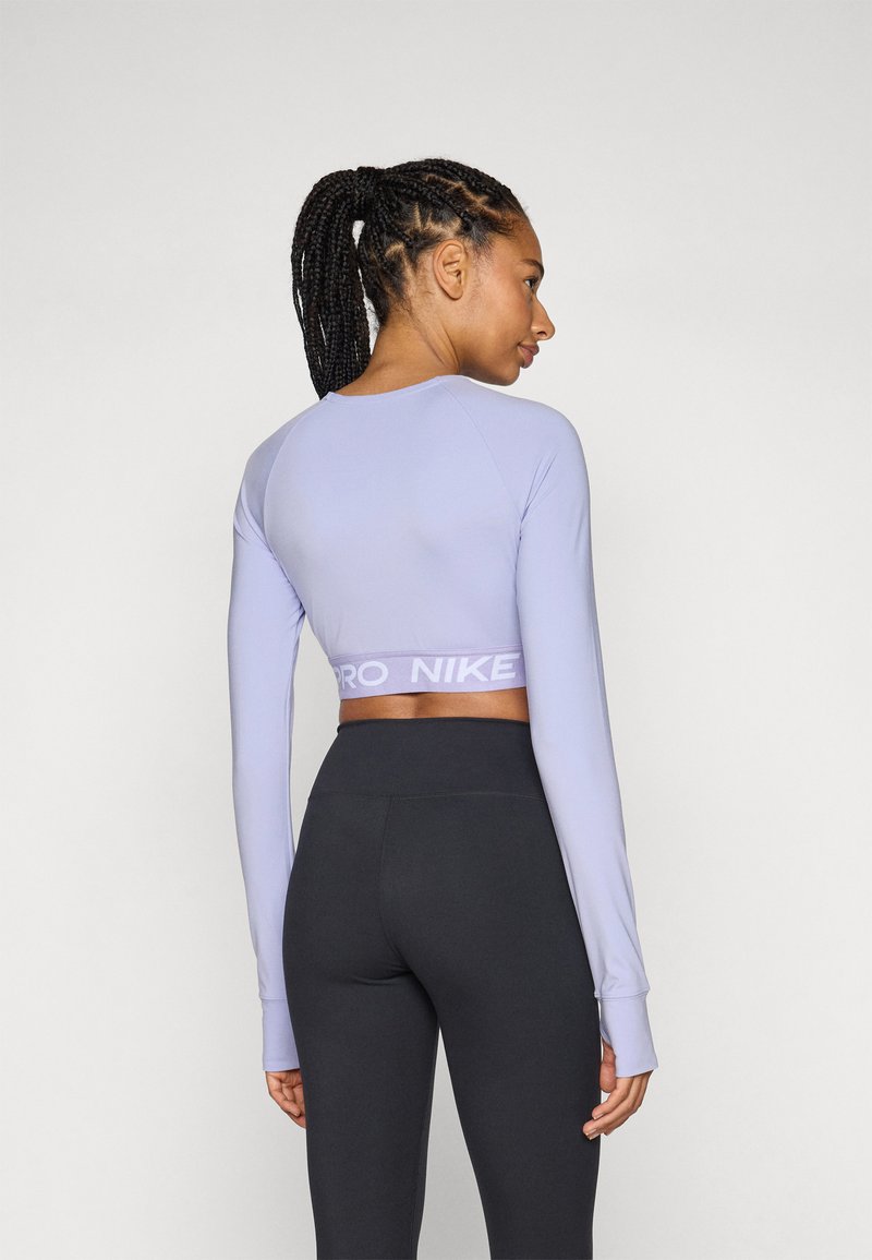 Top corto de manga larga morado con una banda elástica de marca, combinado con leggings negros de cintura alta. Textura suave y diseño ajustado.
