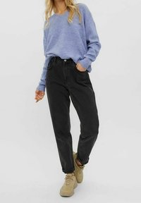 Hellblauer gerippter Pullover, schwarze hoch geschnittene Jeans und beigefarbene Sneakers. Das Outfit zeichnet sich durch einen entspannten Schnitt und ein minimalistisches Design aus.