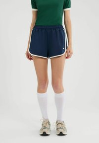 Marineblauwe sportshorts met witte biezen, elastische tailleband en een klein logo. Gecombineerd met een groene shirt en kniesokken in het wit.