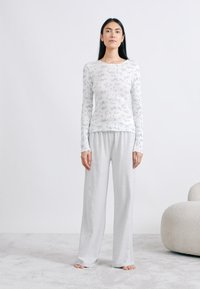 Haut blanc léger à manches longues avec motif floral ; associé à un pantalon ample en coton gris. Texture douce, coupe décontractée, design simple.