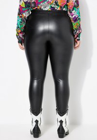 Leggings in ecopelle nera con finitura lucida, silhouette aderente, abbinate a stivali da cowboy bianchi e neri in un design distintivo.