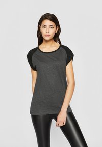Kortermet, rundhalset T-skjorte i mørkegrå med svarte cap sleeves. Mykt materiale med en avslappet passform, kombinert med blanke svarte leggings.