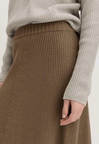 Brauner gerippter Strickrock mit strukturiertem Finish, kombiniert mit einem hellgrauen gerippten Pullover. Der Bund ist eng anliegend und betont die Silhouette.