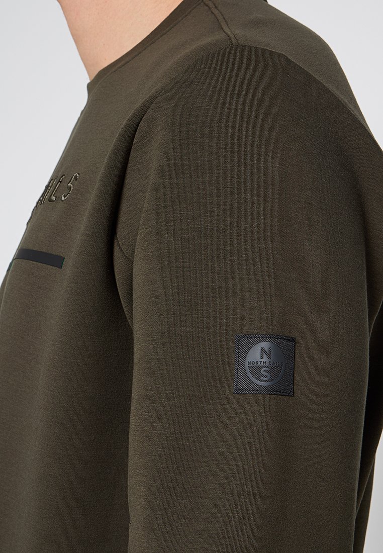 Felpa verde oliva con una texture liscia, caratterizzata da un patch rettangolare nero sulla manica con dettagli del logo e testo ricamato.