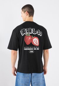 Black cotton t-shirt featuring a large graphic of two strawberries, Japanese text, and the phrase "FRESHNESS ON ME" with a year.