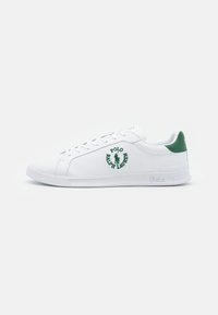 Vita lädersneakers med gröna accenter, med en logotyp på sidan och platta snören. Slät textur och klassisk låg design.