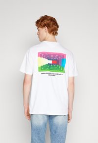 Camiseta blanca de algodón con un gráfico colorido en la parte trasera. El diseño presenta texto en capas de varios colores y la frase "SEPARANDO PAZ Y AMOR."