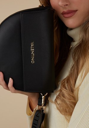 Sac noir en cuir avec un design incurvé, arborant un logo doré "Valentino", une bandoulière détachable et des accents en matériel doré.