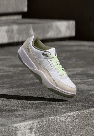 Baskets blanches et beiges avec des lacets vert clair en plein air au-dessus de marches en béton, montrant la semelle et les détails latéraux.