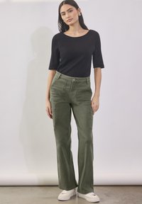 Zwarte top met korte mouwen gecombineerd met olijfgroene cargobroek met zijzakken en een knoopsluiting, gedragen met witte sneakers.