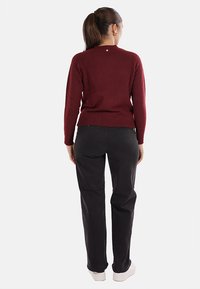 Maglione a maglia bordeaux con scollo rotondo, maniche lunghe e un sottile dettaglio sulla schiena, abbinato a pantaloni neri a gamba dritta e scarpe bianche.
