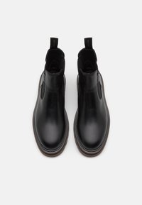 Bottes à chevilles en cuir noir avec panneaux latéraux élastiques et languettes de tirage. Bout arrondi et semelle en caoutchouc texturée pour une meilleure adhérence et un confort optimal.