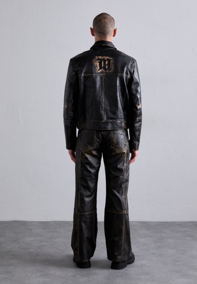 Veste en cuir noir et pantalon large assorti, avec des accents délavés et un logo dans le dos, surface texturée et couture traditionnelle.