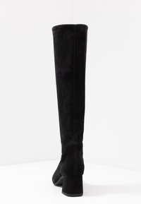 Schwarze Wildleder-Stiefel über das Knie mit einem Blockabsatz, die eine glatte Textur und sichtbare Nahtdetails auf der Rückseite aufweisen.