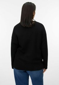 Czarny sweter o luźnym kroju, z długimi rękawami i ribbowanym wykończeniem. Noszony z niebieskimi dżinsami, ukazując gładką teksturę i minimalne detale.