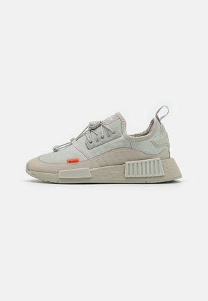 Sneaker Adidas grigio chiaro con suola strutturata, lacci elastici, linguetta sul tallone e piccolo logo arancione sul lato.