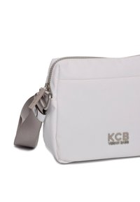 Witte vegan leren tas met een rechthoekige vorm, ritssluiting en een afneembare grijze schouderriem. Kenmerkt het logo "KCB VEGAN BAGS" in zilver.