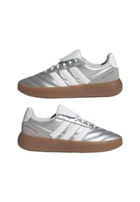 Baskets argentées avec une tige en cuir texturé, un design blanc à trois bandes et une semelle en caoutchouc gomme. Dotées d'une fermeture à lacets et d'une languette rembourrée.