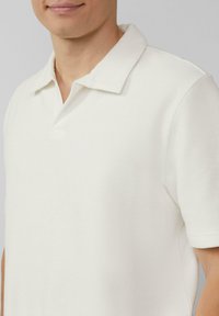 Witte polo met een textuur, voorzien van een klassieke kraag en korte mouwen, getoond vanaf de schouders omhoog.