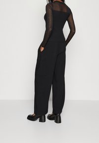 Svart långärmad topp med genomskinliga meshaxlar och prickiga detaljer. Matchas med svarta vida byxor med sidofickor och en avslappnad passform.