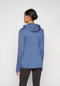 Manta com capuz em um tom de azul médio, feita de um tecido leve. Apresenta mangas longas, um corte descontraído e uma bainha com fenda.