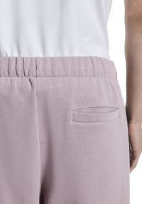 Hellviolette Jogginghosen mit elastischem Bund und einer kleinen aufgenähten Tasche auf der Rückseite. Weicher, strukturierter Stoff mit lockerem Schnitt.