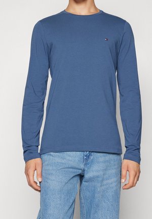 Long-sleeve shirt in a soft blue fabric with a fitted design, rounded neckline, and small logo accent on the chest.