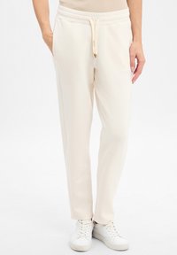 Pantalons de survêtement beige clair avec une taille �à cordon, poches latérales et une texture douce. Associés à des baskets blanches.