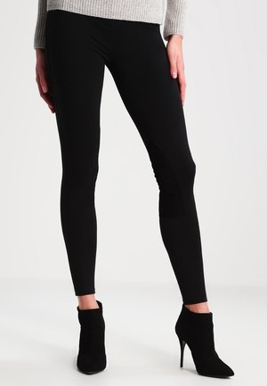 Leggings dengan tambalan tekstur di lutut dipadukan dengan sepatu bot pergelangan kaki hak tinggi hitam dan sweater rajut berwarna terang.