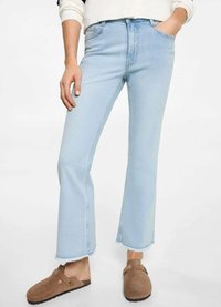 Jeans de mezclilla azules claros con campana y dobladillo sin acabar, diseño de cinco bolsillos y ligero desgastado. Combinados con zapatos marrones tipo slip-on.