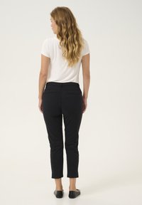 Pantaloni neri a culotte con una vestibilità slim, caratterizzati da una finitura liscia e due tasche posteriori. Abbinati a una t-shirt bianca e a scarpe basse.