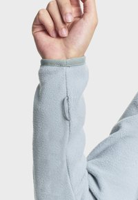 Svijetloplav duks s dugim rukavima, pufastih manžeta koje su ugodne na dodir. Na zapešću se nalazi sivi detalj i mala petlja za podršku palcu.