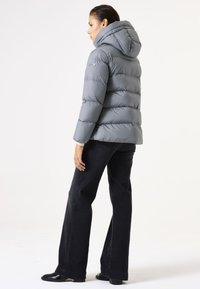 Grijze pufferjack met capuchon, voorzien van horizontaal gestikte secties en een iets losse pasvorm, gecombineerd met zwarte wijde jeans.