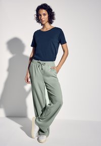 Mörkblå t-shirt med korta ärmar i kombination med ljusgröna vida byxor med elastisk midja och dragsko, tillsammans med vita sneakers.