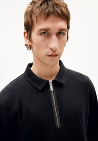 Schwarzer Reißverschluss-Pullover mit strukturiertem Muster, Kragen und auffälligem Metallreißverschluss. Hat eine enge Passform und weichen, gewebten Stoff.